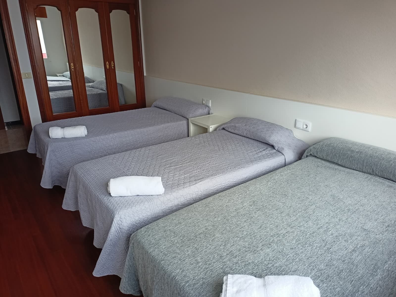 A hotel room with three single beds, each with a grey bedspread and white towels.