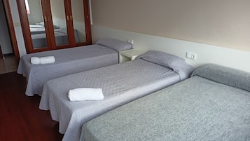 A hotel room with three single beds, each with a grey bedspread and white towels.