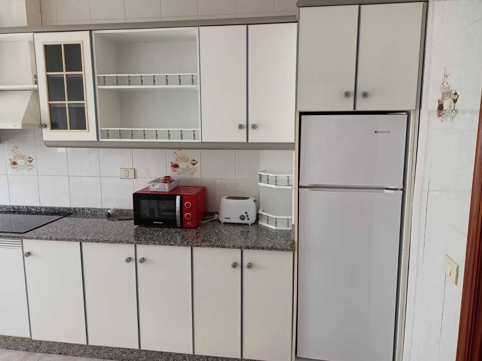 Een keuken met witte kastjes, een rode magnetron, een witte broodrooster en een witte koelkast.
