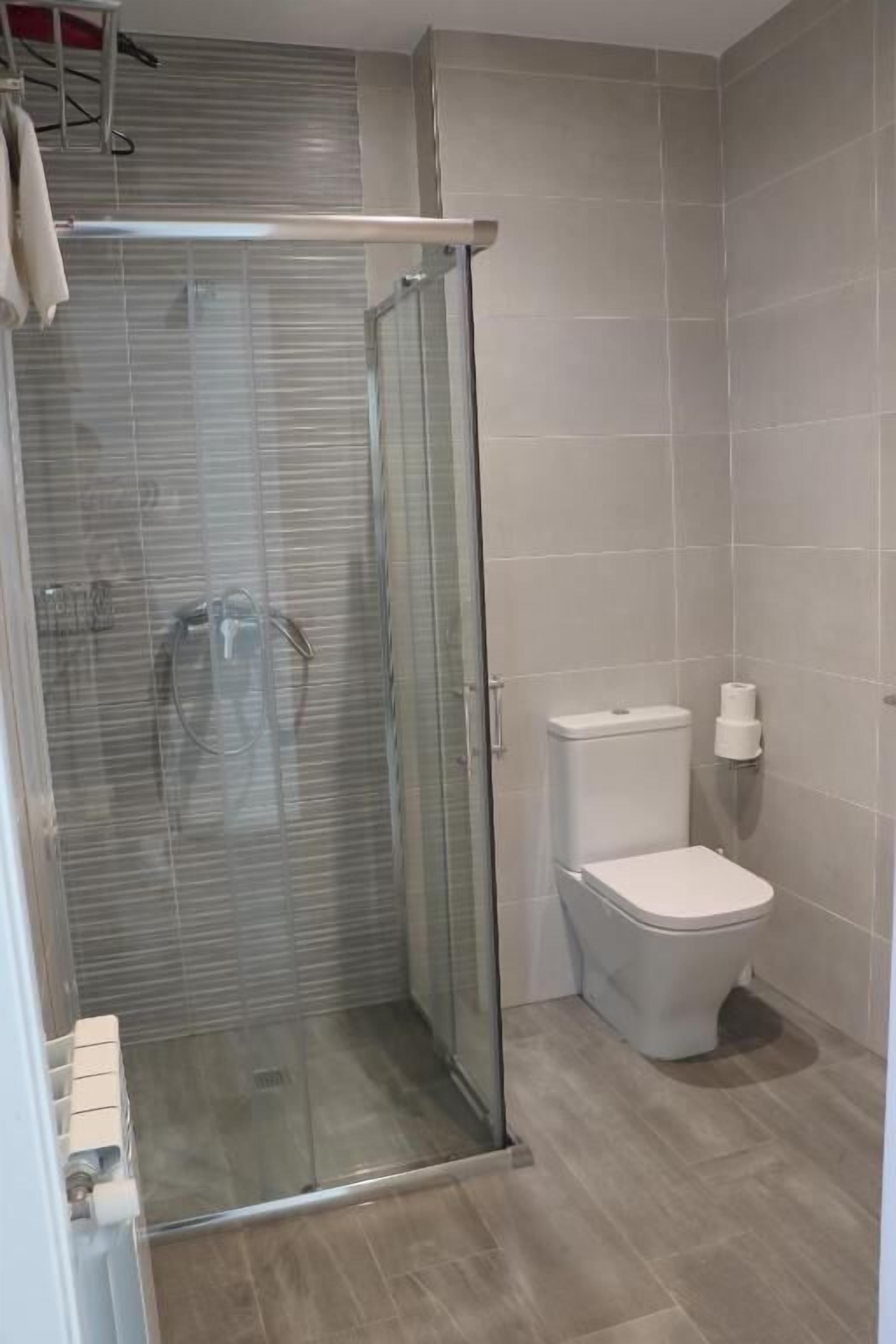 Casa de banho com cabine de duche em vidro, sanita e suporte para toalhas.