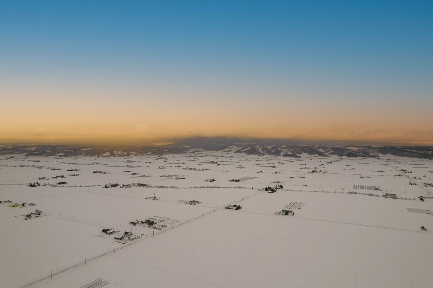 A vast snowy landscape with scattered buildings and fields.