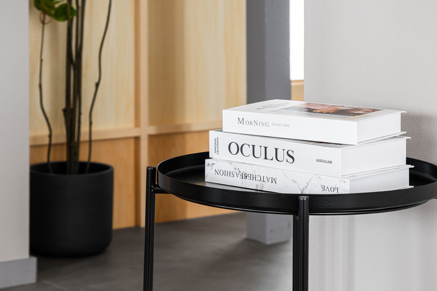 A stack of books on a black table with a potted plant in the background.