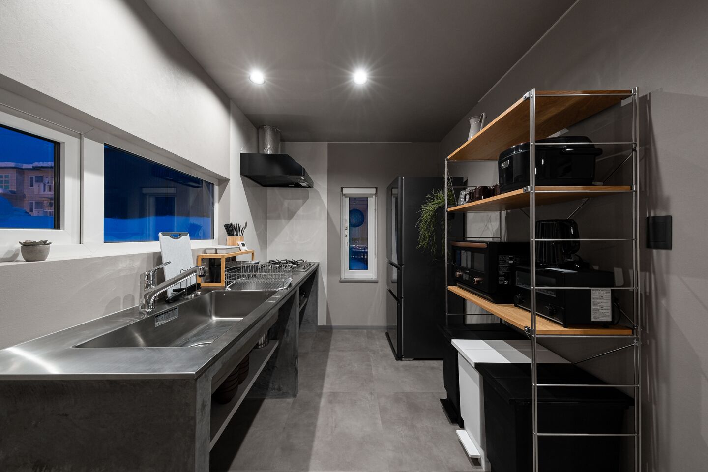A modern kitchen with a stainless steel sink, a stove, and a built-in oven. There is a window providing a view of the outside, and a black refrigerator with a built-in microwave.