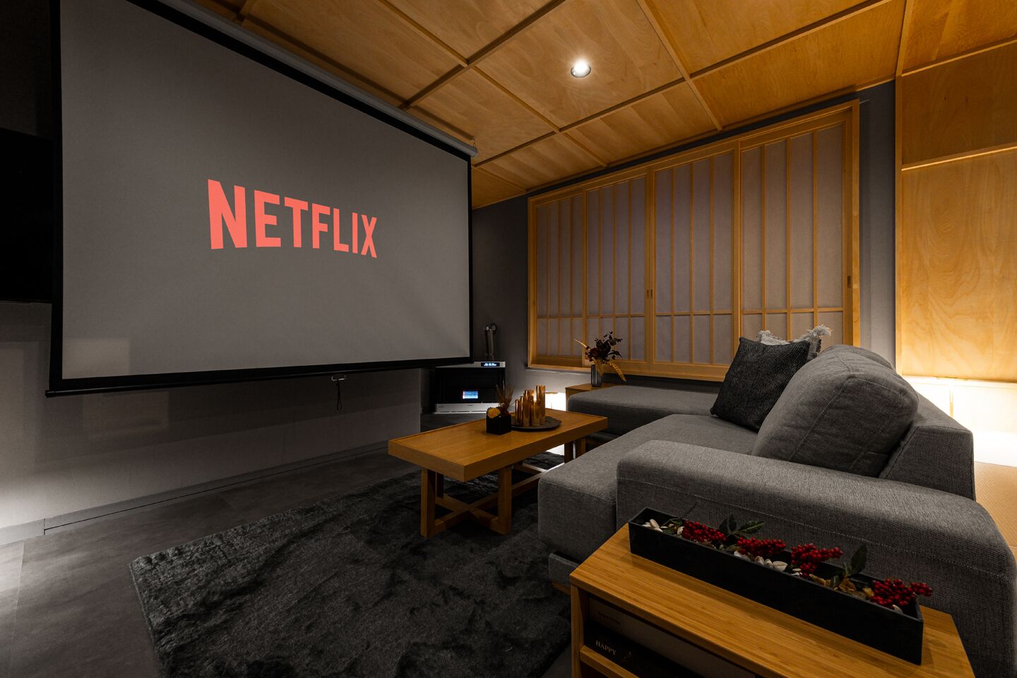 A modern living room with a large flat-screen TV displaying "NETFLIX," a sofa, a coffee table, and a wooden cabinet.