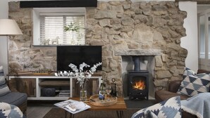 A cozy living room with a stone fireplace, a flat-screen TV, and a comfortable seating area. - Rosehendra - A beautifully refurbished pet-friendly barn conversion with two bedrooms, a log burner (Rosevidney)