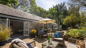 A cozy outdoor patio with wicker furniture, a stone building, and a variety of plants. - Rosehendra - A beautifully refurbished pet-friendly barn conversion with two bedrooms, a log burner (Rosevidney)