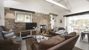 A cozy living room with a stone wall, a fireplace, a television, and comfortable seating. - Rosehendra - A beautifully refurbished pet-friendly barn conversion with two bedrooms, a log burner (Rosevidney)