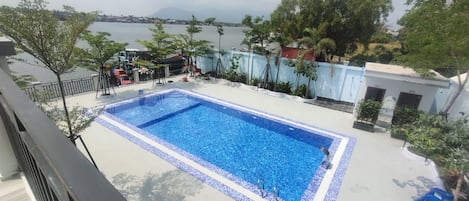 Una piscina rectangular con borde de azulejos, rodeada por un muro bajo y árboles.