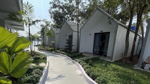 Un chemin mène à une série de bâtiments modernes, blancs, à l’architecture incurvée, entourés d’une végétation luxuriante et de palmiers.