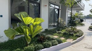 Un bâtiment moderne doté de grandes fenêtres, d’un jardin bien entretenu avec différentes espèces de plantes et d’un chemin en béton.