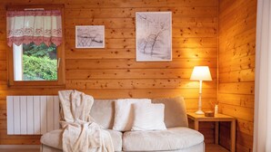 Tunnelmallinen huone, jossa on puuseinä, valkoinen patteri, beigenvärinen sohva, jossa on peitto, sekä lamppuvarustettu pöytä.