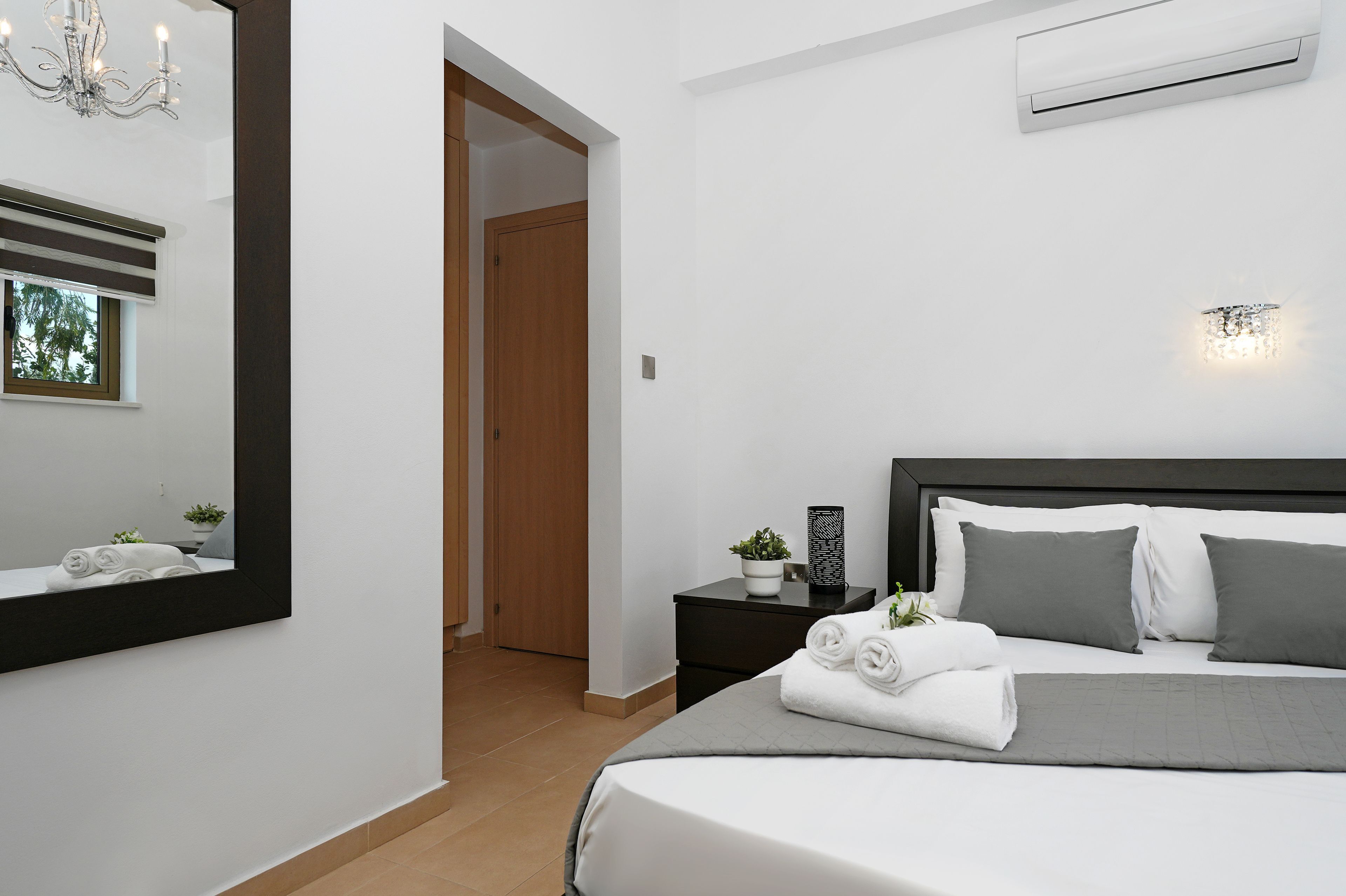 A modern bedroom with a bed, bedside tables, a mirror, and an air conditioning unit.