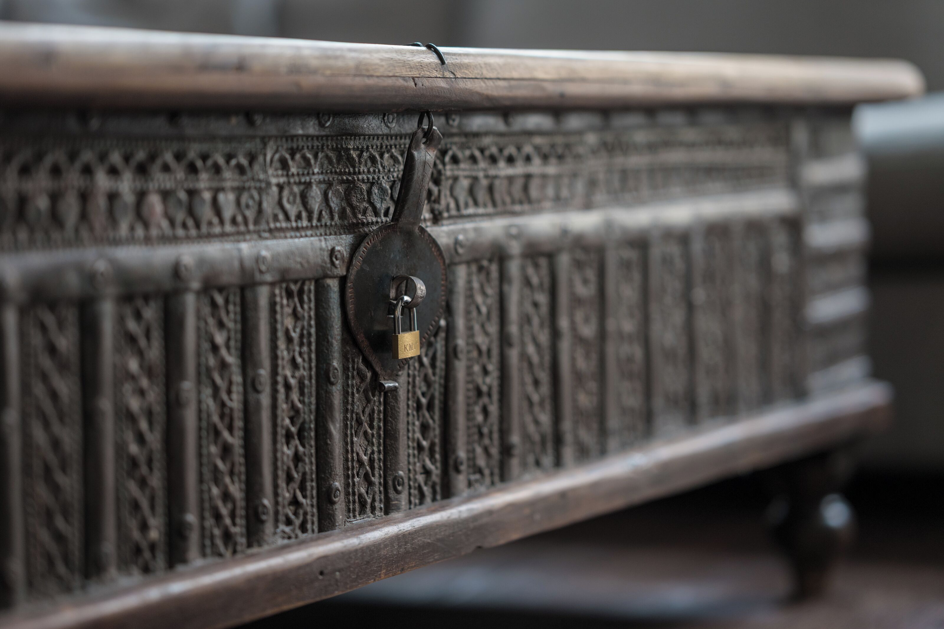 A close-up of a metal bed frame with intricate carvings and a padlock.