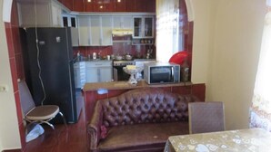 Une cuisine compacte équipée d’un réfrigérateur, d’une cuisinière et d’un four à micro-ondes. On y trouve un canapé et une table à manger recouverte d’une nappe à motifs.