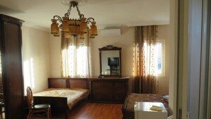 Une chambre avec un plancher en bois, un lit, un bureau, une chaise, une commode, un miroir et un lustre.