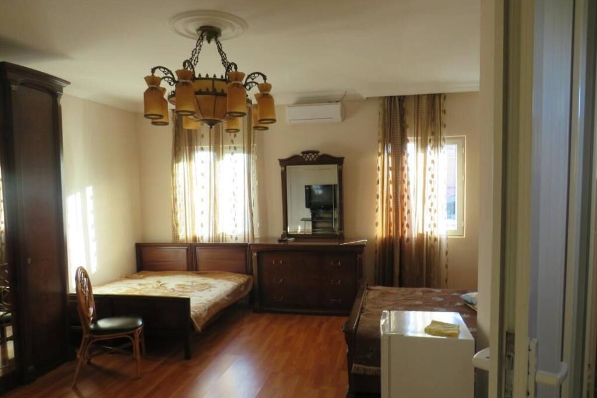 Un dormitorio con piso de madera, una cama, un escritorio, una silla, un aparador, un espejo y una araña.