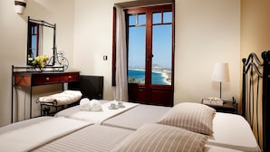 Een hotelkamer met een bed, een bureau met spiegel, een lamp en uitzicht op zee.
