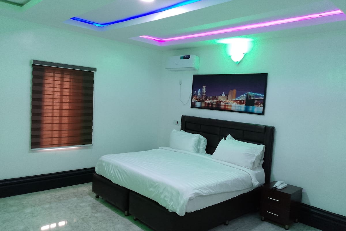 A bedroom with a bed, a nightstand, a wall-mounted air conditioner, and a cityscape painting.