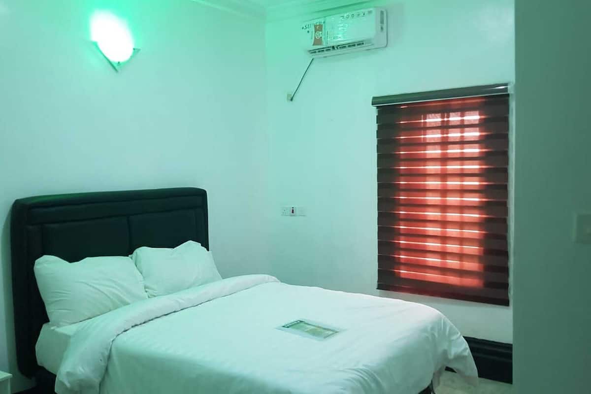A bedroom with a bed, a window with blinds, an air conditioning unit, and a light fixture.
