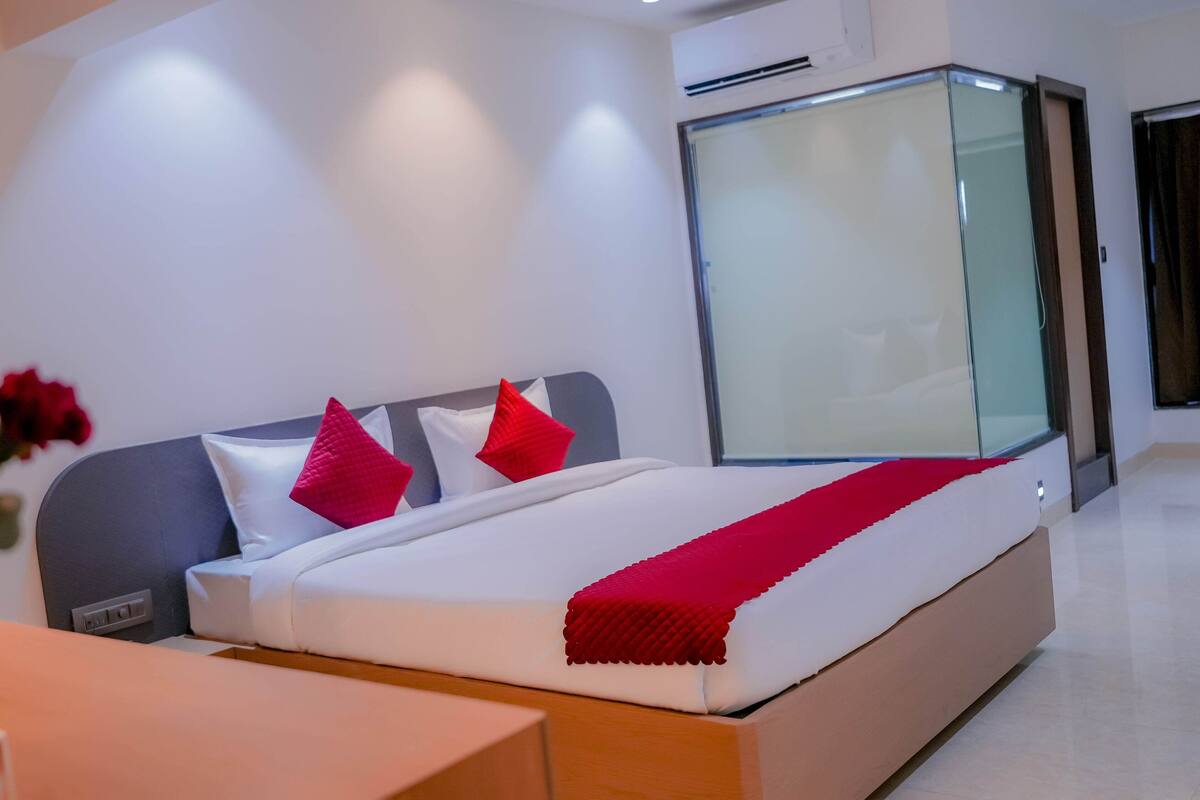 A modern hotel room with a large bed, a bedside table, and a glass partition wall.