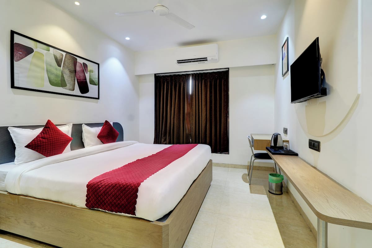 A hotel room with a bed, a desk, a TV, and an air conditioning unit.