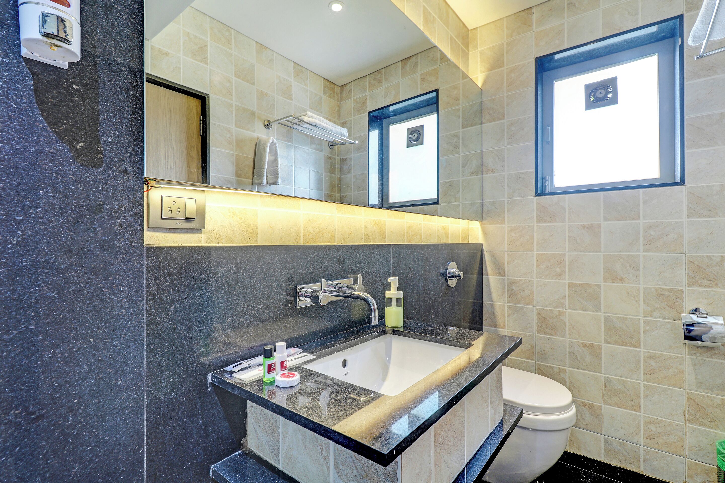 A modern bathroom with a granite countertop sink, a mirror, a towel rack, and a toilet.