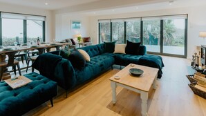 A spacious living area with a large sectional sofa, a dining table set for four, and a view of the outdoors through large windows.