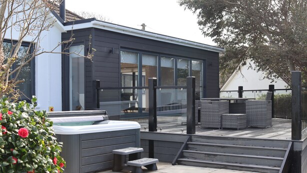 A modern house with a hot tub, outdoor seating, and a staircase leading to a deck.
