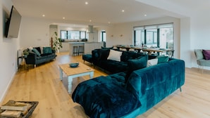 A modern living room with a dark teal sofa, a wooden coffee table, and a kitchen in the background.