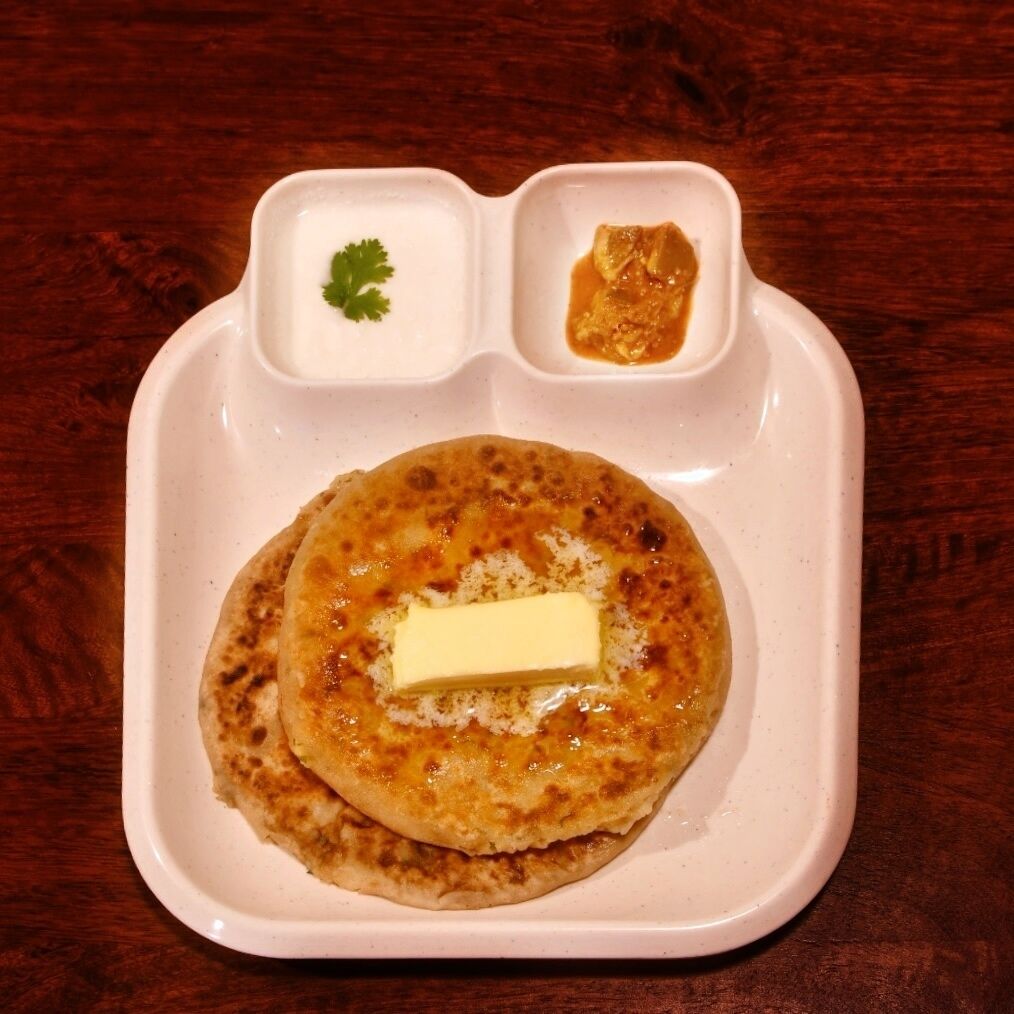 A plate with two pancakes, a dollop of butter, and two small containers of condiments.