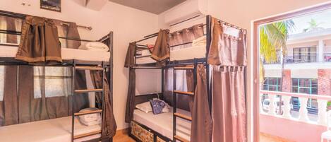 Une chambre de dortoir avec des lits superposés, une fenêtre avec des rideaux et des affiches sur le mur.