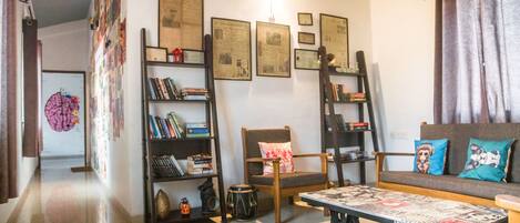 A living room with a sofa, a coffee table, a bookshelf, a chair, and a wall with framed pictures.