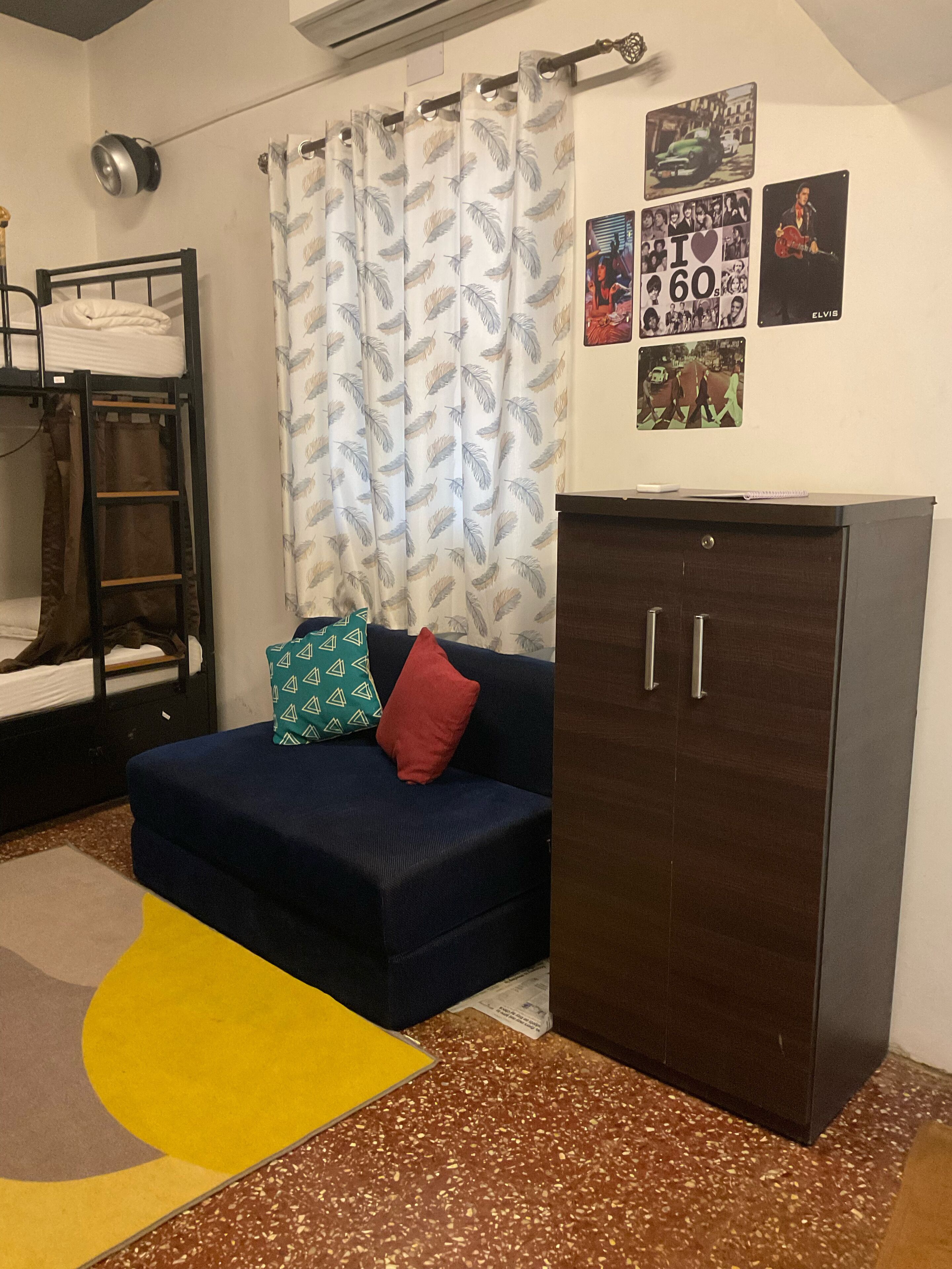 Una habitación tipo dormitorio con una cama litera, un sofá azul con almohadones, un armario y adornos en la pared.