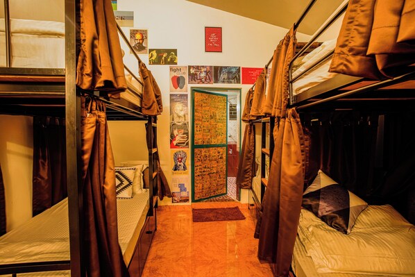 A dormitory room with bunk beds, a door with posters, and a small rug on the floor. - U.R.D.Ki You are the key Hostels (Anjuna)