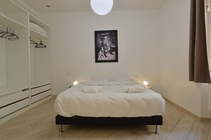 A bedroom with a bed, bedside lamps, a wardrobe, and a framed picture on the wall.