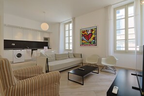 A modern living room with a sofa, chairs, a coffee table, and a kitchen area with a washing machine.