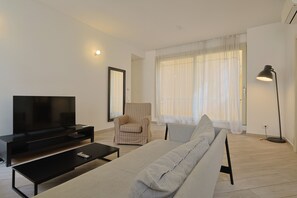 A modern living room with a flat-screen TV, a sofa, a chair, and a floor lamp.