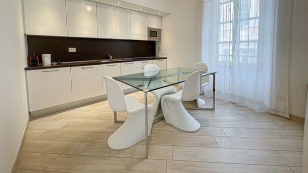 A modern kitchen with white cabinets, a glass dining table, and white chairs.