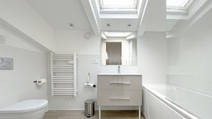 Ein modernes Badezimmer mit Dachfenster, Toilette, Waschbecken inklusive Spiegel und Dusche.