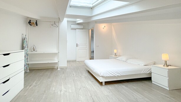 Ein modernes Schlafzimmer mit Dachfenster, einem Bett, einem Nachttisch, einer Kommode und einem Kleiderschrank.