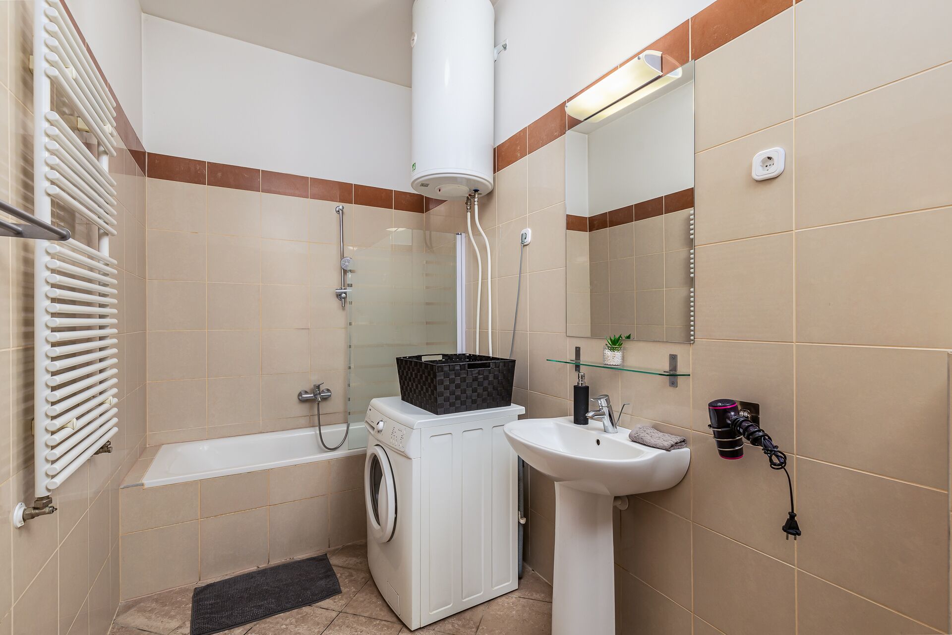 A modern bathroom with a washing machine, a sink, a glass shower enclosure, and a towel rack.