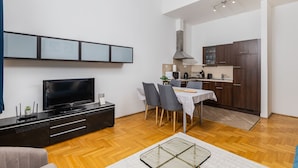 A modern living room with a flat-screen TV, a dark wooden entertainment unit, and a dining area with a table and chairs. - Venus Apartments - Gozsdu Court III (Budapest)