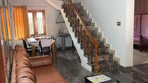 Ein Wohnzimmer mit einem braunen Ledersofa, einem schwarzen Couchtisch mit Papieren, einer Treppe mit Holzspindeln und einem Essbereich im Hintergrund.