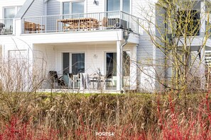 A two-story house with a balcony, a dining area with chairs and a table, and a garage door. - Stjernehus - Ground Floor, Infrared Sauna, Fireplace, Washing Machine, Terrace (Olpenitz)