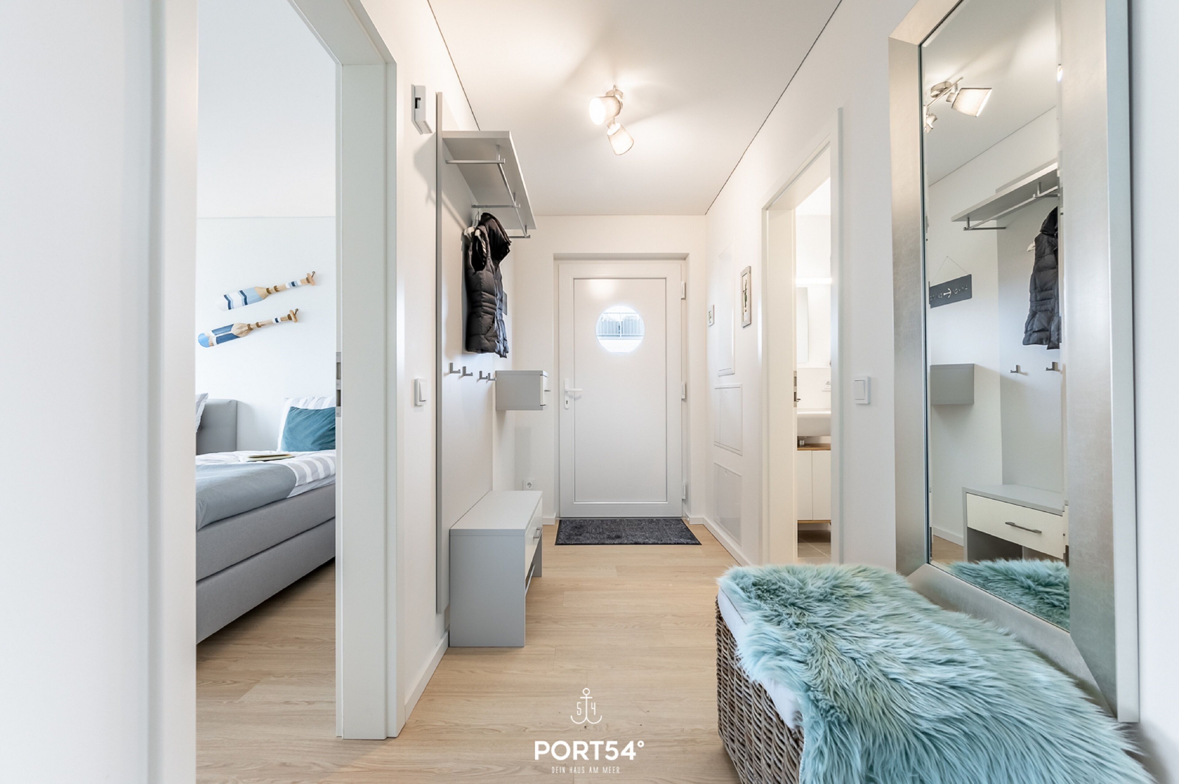 A modern, well-lit hallway with a grey sofa, a bench, and a mirror reflecting a coat rack.