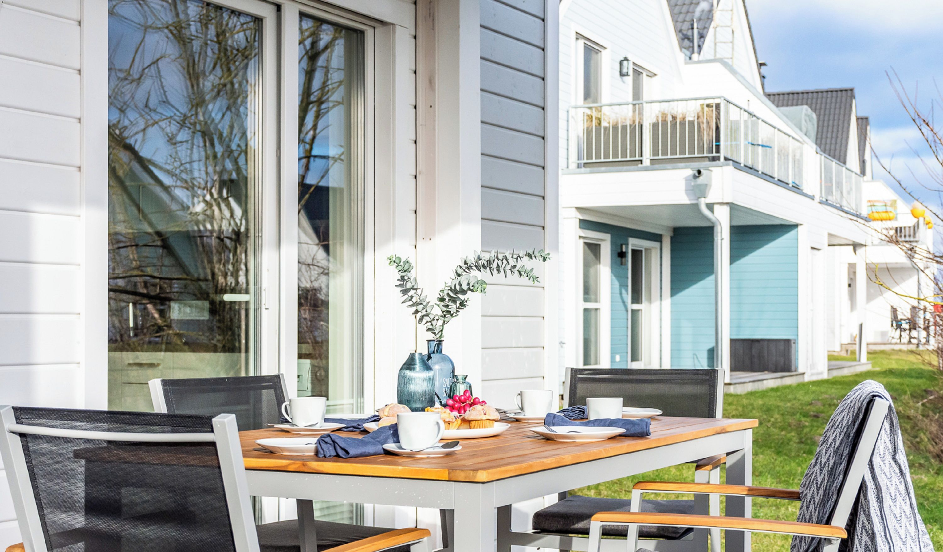 A dining area with a wooden table and chairs, a vase with flowers, and a window with a view of the building's exterior.