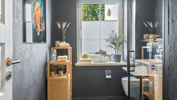 Ein modernes Badezimmer mit Holzboden, einer Duschkabine aus Glas und einem Fenster mit Blick auf Grünflächen.