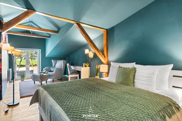 A bedroom with a sloped ceiling, a bed with a green textured blanket, a desk with a chair, and a window with a view of greenery. - "luxuriöser Aufenthalt in der Wohnung "hummer" auf dem Majorshof" (Hedwigenkoog)