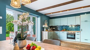 Una cocina moderna con armarios azul claro, un ventanal grande y una zona de comedor con mesa de madera y plantas en macetas.
