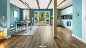 Una cocina moderna con vigas de madera, un comedor con mesa y sillas, y vista a un jardín a través de puertas de vidrio.